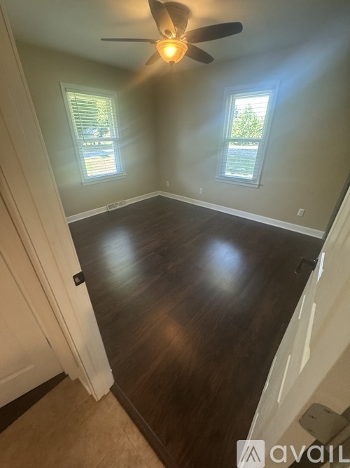 A room with a ceiling fan and two windows.