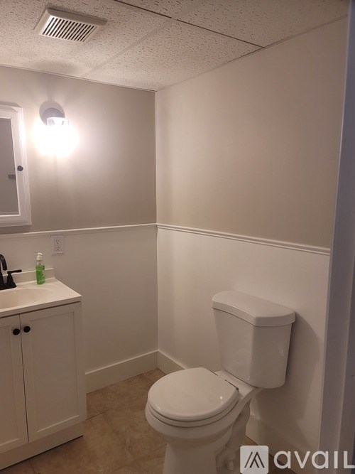 A white toilet in a small bathroom with a cabinet and a light on.