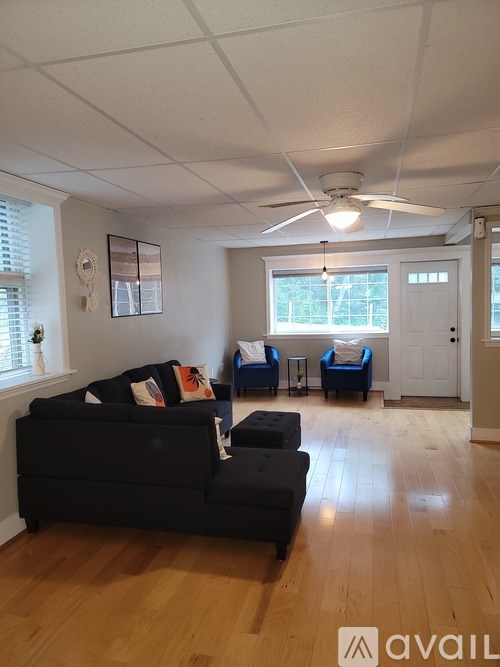 A living room with a black couch and a fan on the ceiling.