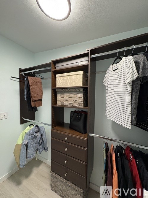 A closet with clothes hanging and a shelf with baskets.