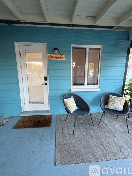 A blue house with a white door and a window with a brown pillow on a chair.