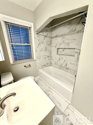 A white sink with a silver faucet in a bathroom with a marble wall.
