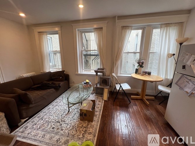 A living room with a brown couch, a glass coffee table, and a white refrigerator.
