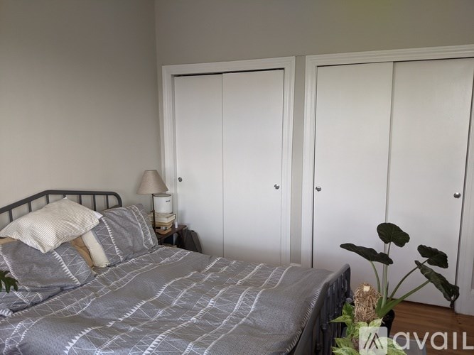 A bed with a grey comforter and a white pillow is in the foreground of a room with two white doors.