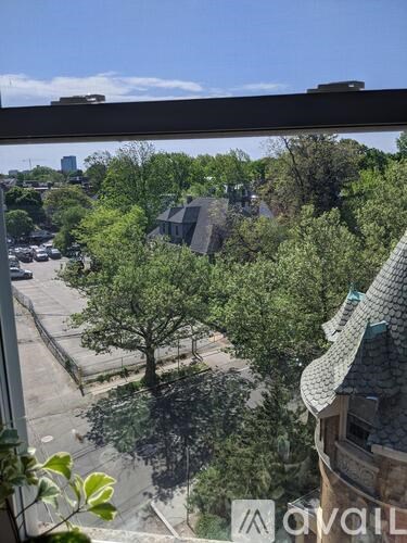 A view from a window looking out at a tree, a building, and a parking lot.