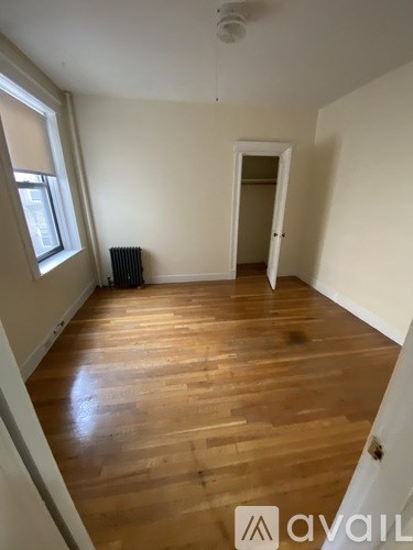 A room with wooden flooring and a window on the left side.
