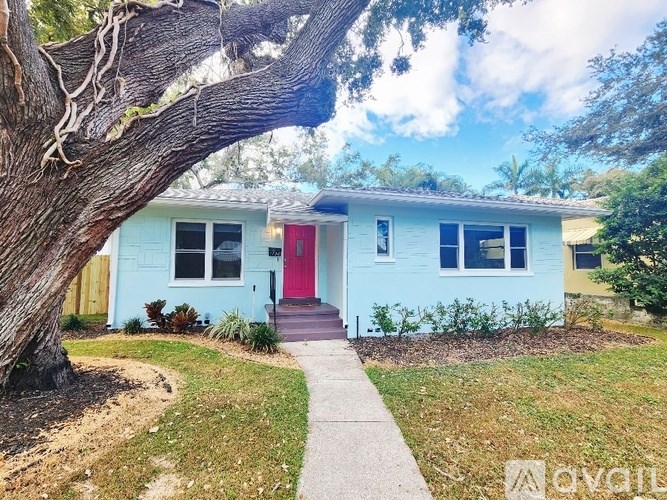 A blue house with a red door and a tree in front.