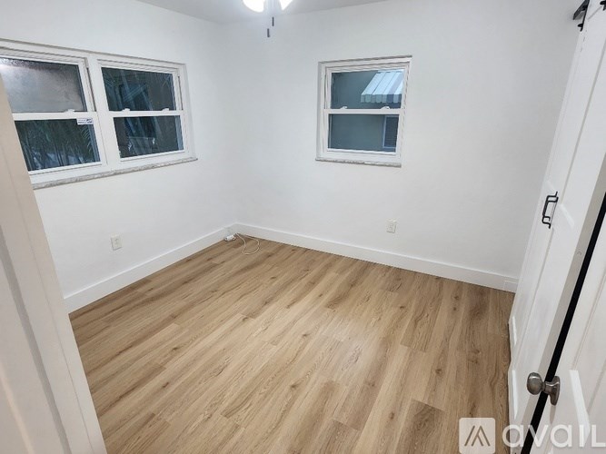 A room with wooden flooring and two windows.