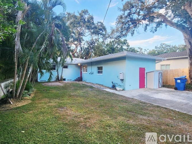A blue house with a red door is surrounded by greenery.