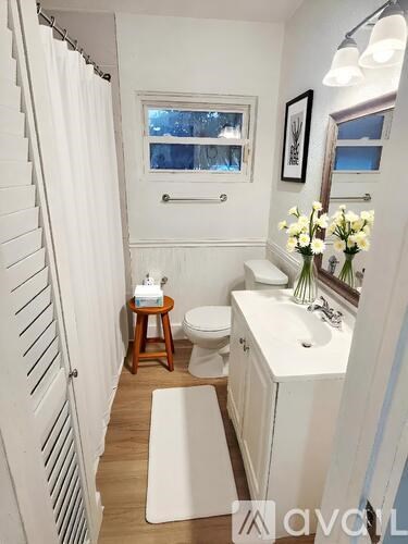 A small white bathroom with a toilet, sink, and a window.