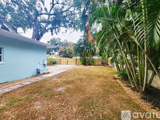 A blue house with a brick pathway leading to a fence and trees.
