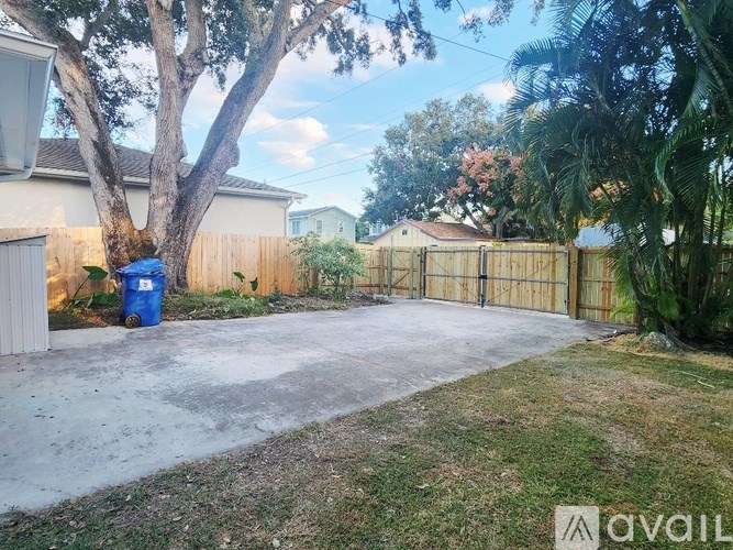 A backyard with a fence, a tree, and a blue trash can.