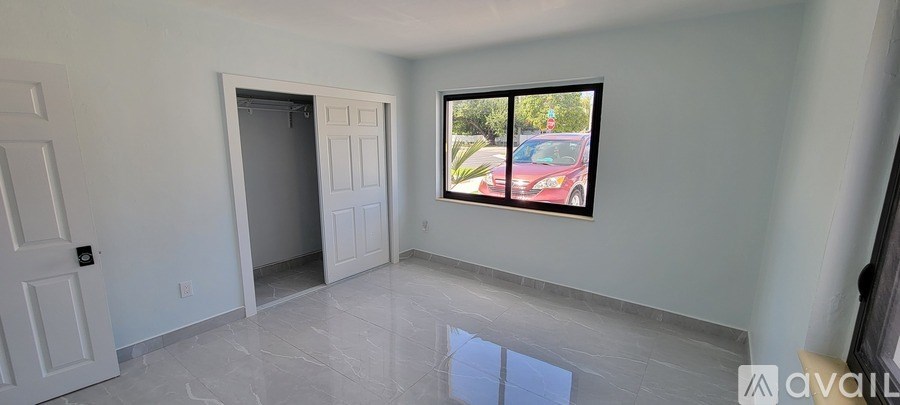 A room with a large window and a door is available for rent.