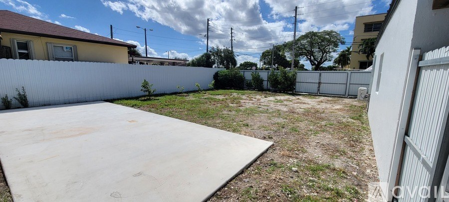 A backyard with a white fence and a white concrete slab.