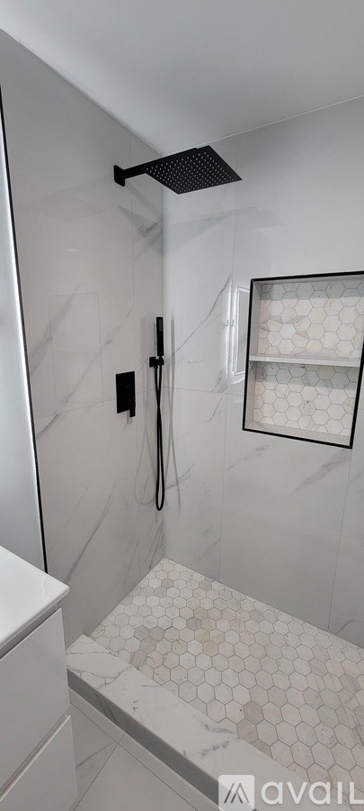 A white tiled shower with a black drain cover.