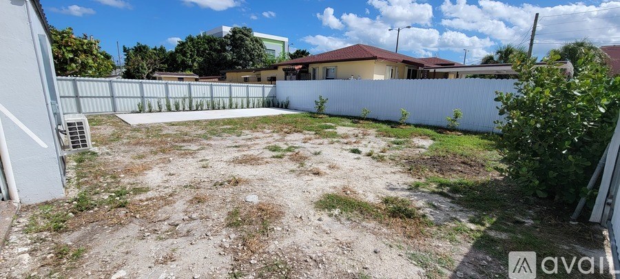 A backyard with a white fence and a house in the background.