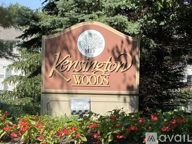 A sign for Kensington Woods surrounded by greenery and flowers.