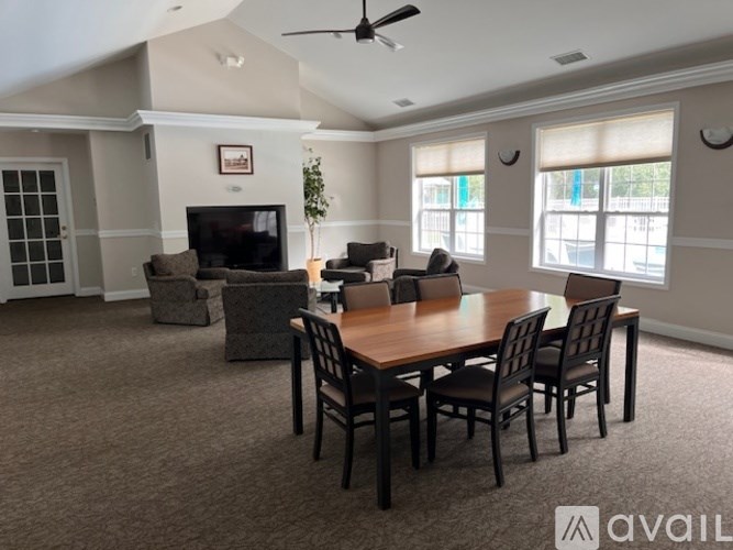 A living room with a brown carpet and a wooden dining table with chairs.