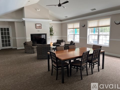 A living room with a brown carpet and a wooden dining table with chairs.
