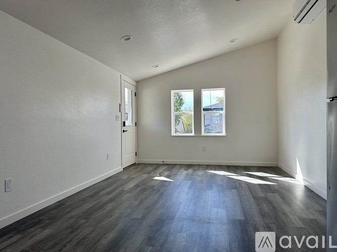 A spacious room with wooden flooring and a window showing a view of a building outside.