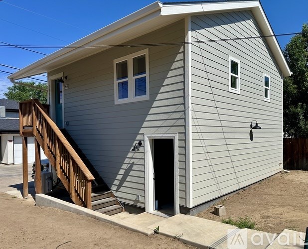 A small house with a grey siding and a brown wooden staircase.