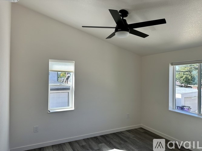A room with a ceiling fan and two windows.