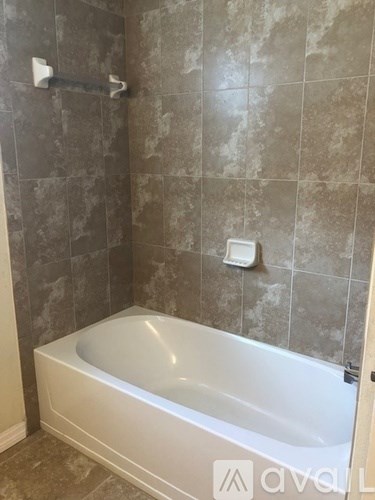 A bathroom with a white bathtub and grey tiles.