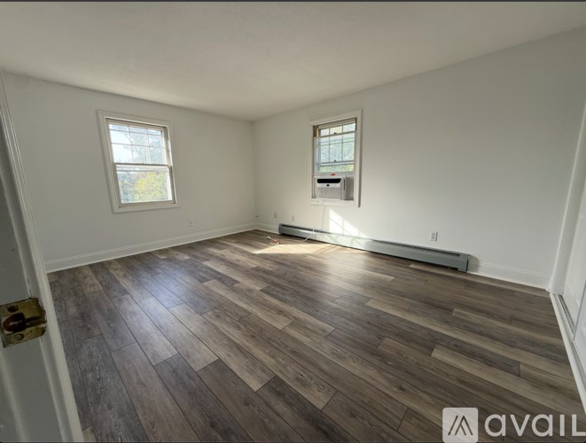 A room with wooden flooring and two windows.