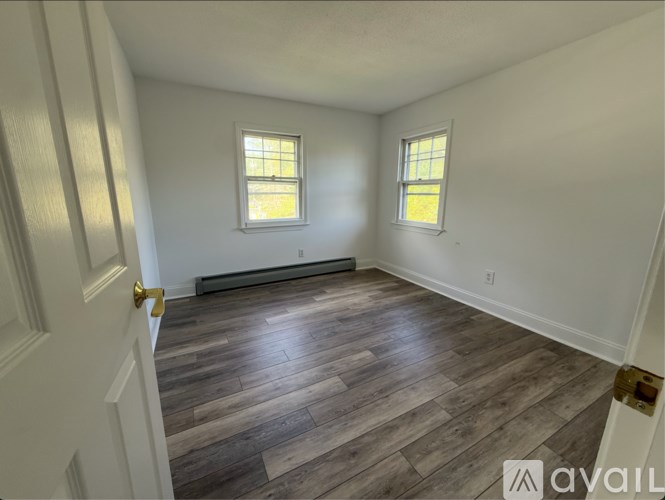 A room with wooden flooring and two windows.