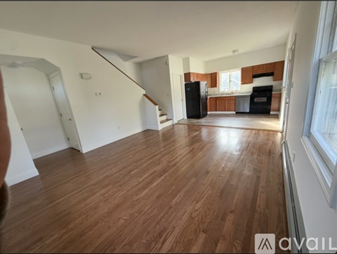 A spacious living room with wooden flooring and a kitchen area in the background.