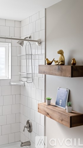 A bathroom with a white tiled shower and a wooden shelf with a tablet and plants on it.
