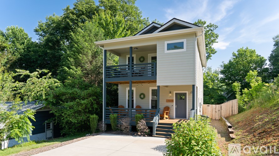 A two-story house with a balcony on the second floor is surrounded by greenery.
