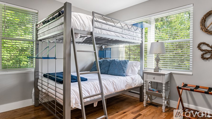 A white bunk bed with a ladder is in a room with a window and a table.
