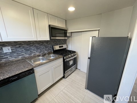 A kitchen with a black fridge, white cabinets, and a black countertop.