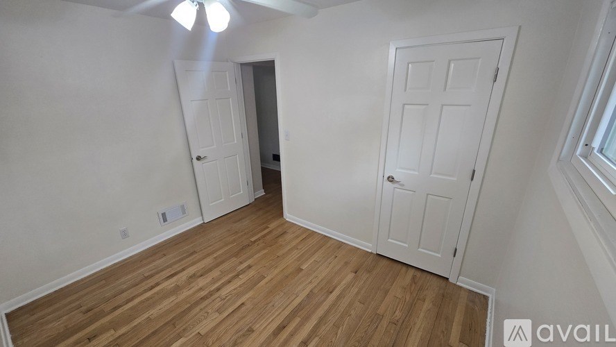 A room with wooden floors and white walls, featuring a ceiling fan and two doors.