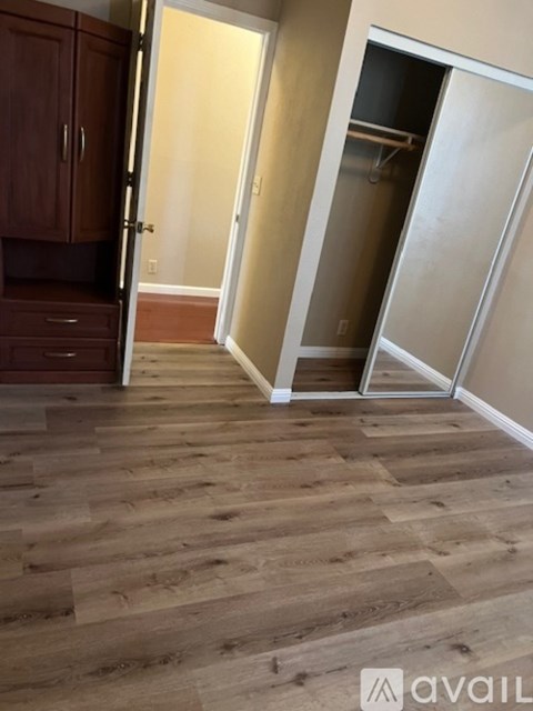 A kitchen with wooden floors and cabinets with a door open.