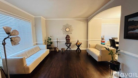 A living room with a white sofa, a wooden floor, and a painting on the wall.