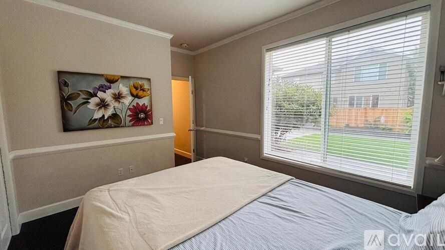 A bedroom with a bed, a painting on the wall, and a window with blinds.