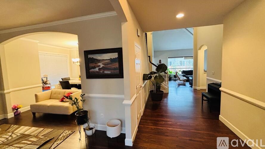 A living room with a couch, a rug, a painting, and a hallway leading to a balcony.