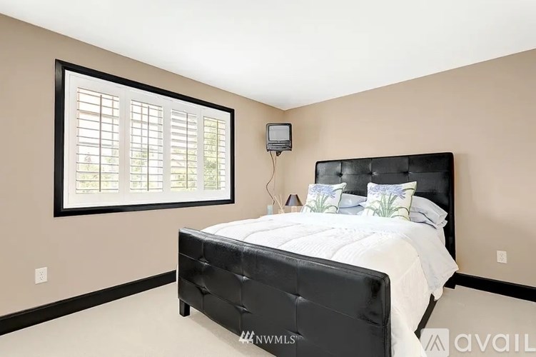 A bedroom with a black bed and a window with blinds.