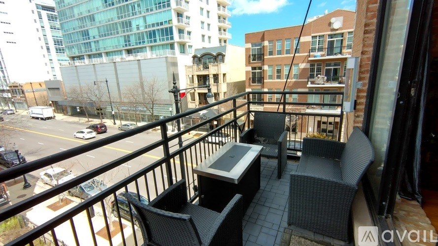 A balcony with a table and two chairs overlooks a city street.