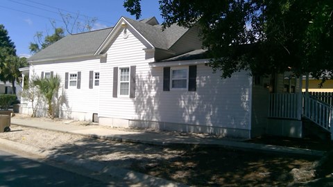 A white house with a grey roof and a tree in front.