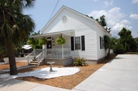 A white house with a porch and a tree in front.