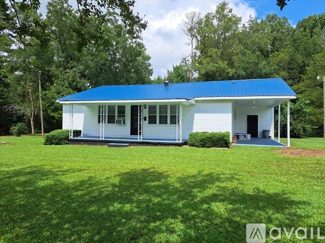 A white house with a blue roof is surrounded by greenery.