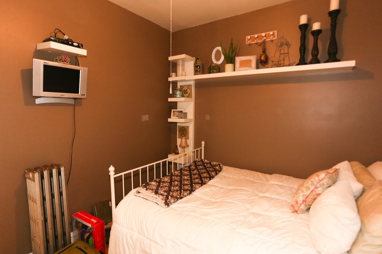 A bedroom with a bed, shelves, and a microwave.