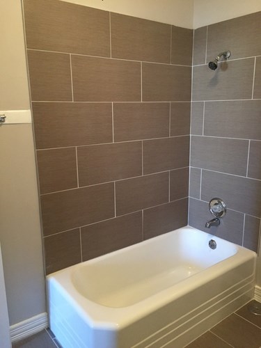 A white bathtub is in a bathroom with brown tiles.