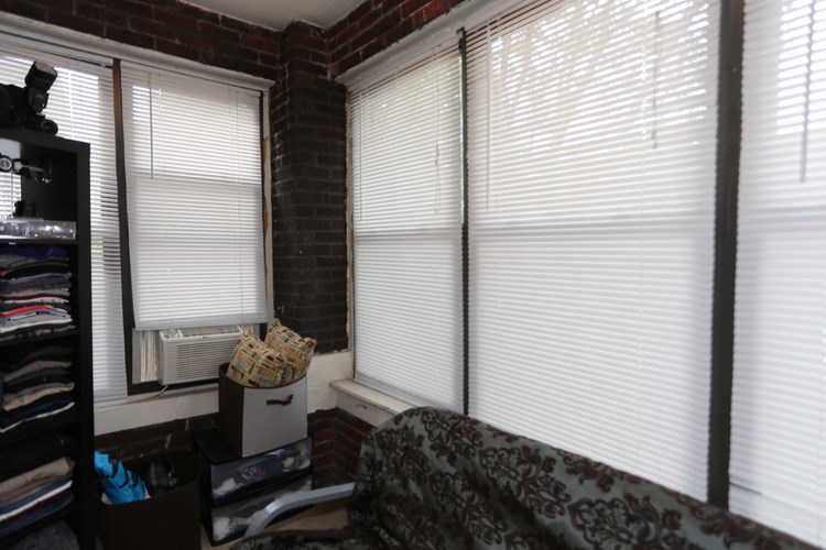 A room with a window covered in blinds and a chair with a patterned cushion.