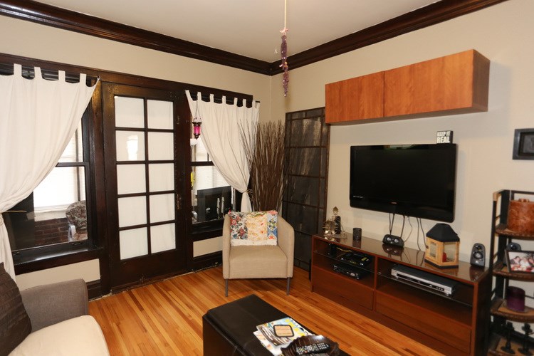 A living room with a wooden floor and a flat screen TV mounted on the wall.