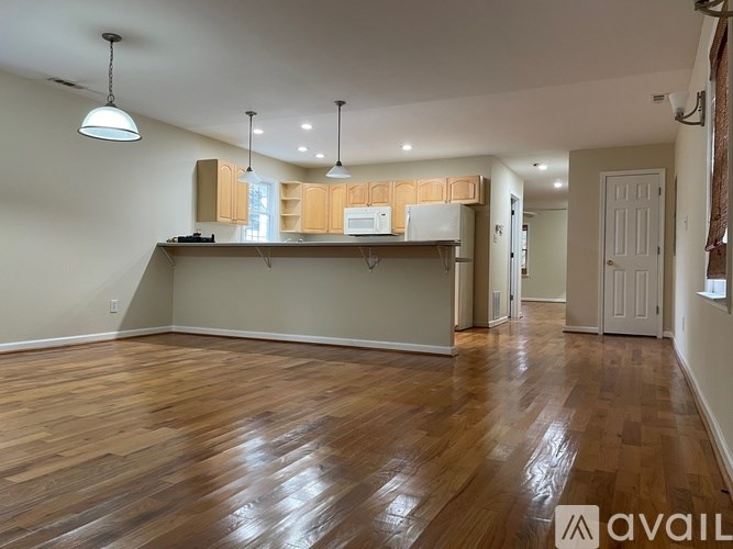 A spacious room with wooden floors and a kitchen area in the background.