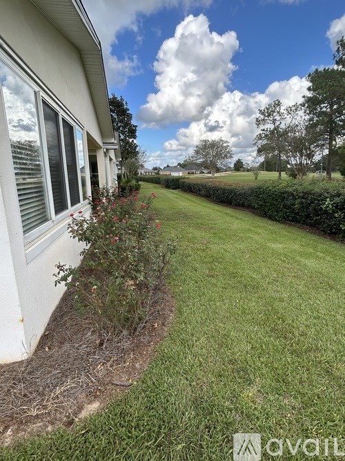 A house with a white siding and a window is shown with a grassy area and a hedge in the foreground.